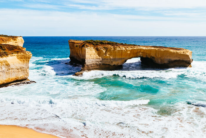 Stunning coastal vista featuring a natural rock formation and turquoise waves under a clear blue sky.