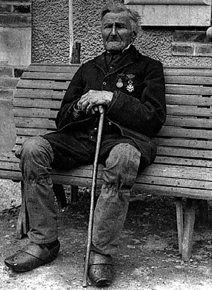 Elderly man with medals sitting on a bench holding a cane in a rare photo of famous historical figures.