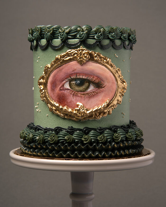 A visually stunning cake with an eye design in a gold frame, featuring intricate green decorations.