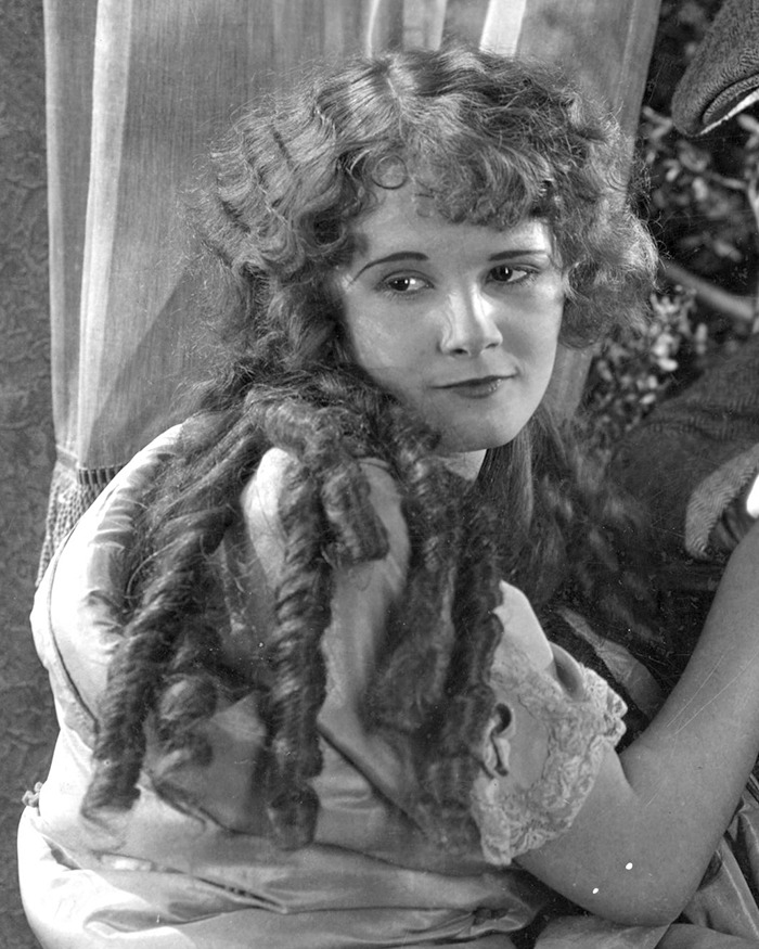 Young female child actor with long curly hair, posing thoughtfully in a vintage setting, representing child actors' early fame.
