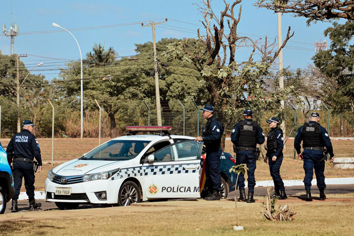 Police officers gathered near a patrol car in a park setting, responding to an incident involving a man and his wife.