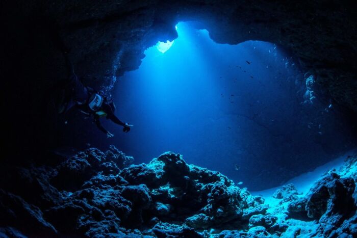 Diver explores a deep ocean cave, surrounded by mysterious rock formations and blue light.