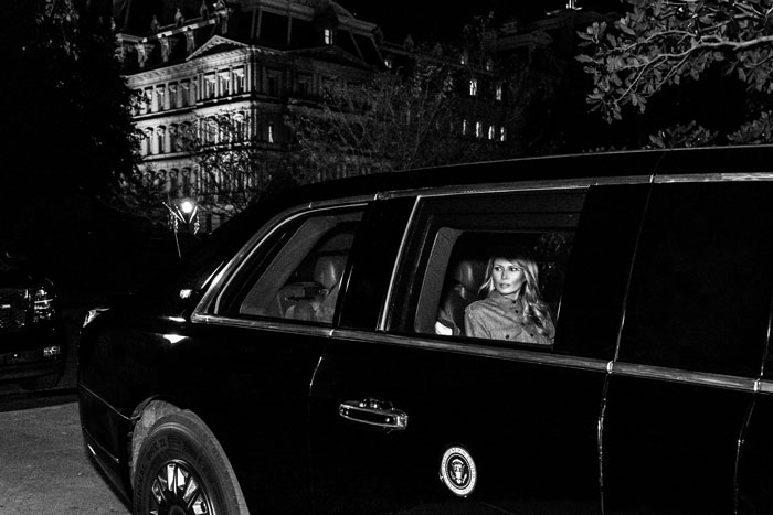 A woman sitting in a black car at night, with a historic building in the background, related to White House events.