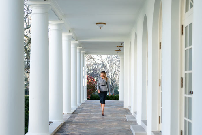 Melania Trump walks through the White House colonnade, showcasing glamorous style.