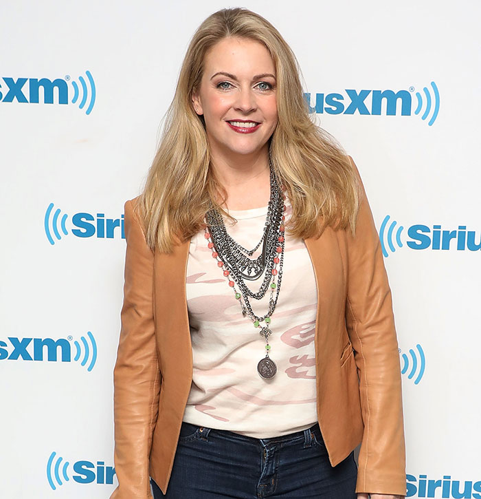 Blonde woman in a leather jacket poses at a SiriusXM event, smiling.