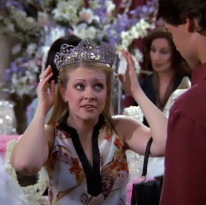 Woman adjusting a tiara at an event, surrounded by floral decorations.