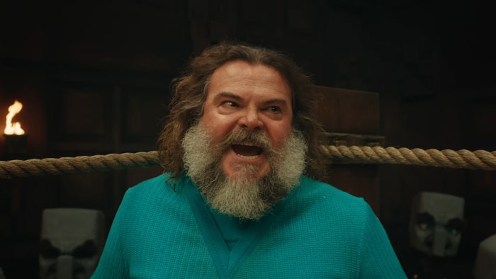 Bearded man in a blue shirt, laughing energetically in a dimly lit room related to Minecraft movie trend.