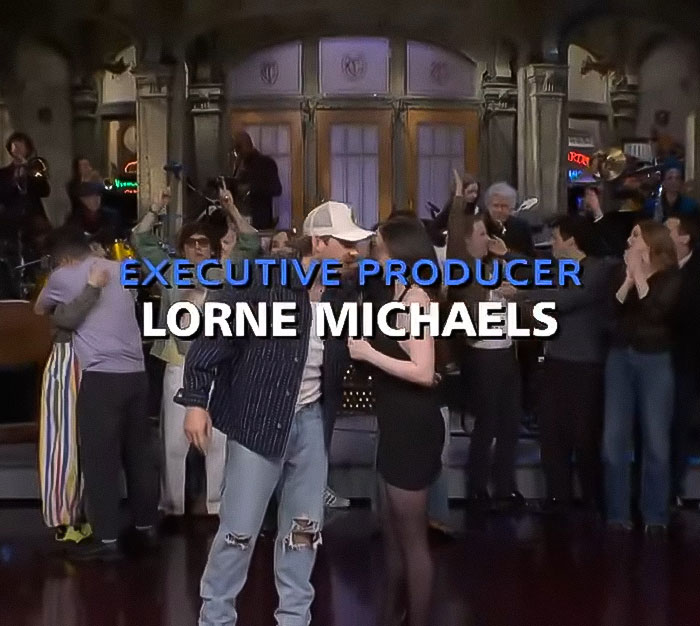 Morgan Wallen on SNL stage, wearing a white cap and denim, with background audience and credits displayed.