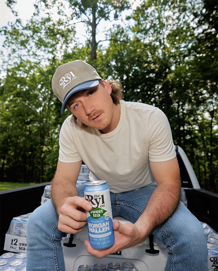 Morgan Wallen in a cap holding a Morgan Wallen branded can of sweet tea outdoors, emphasizing country star wealth. Morgan Wallen in a cap holding a Morgan Wallen branded can of sweet tea outdoors, emphasizing country star wealth.