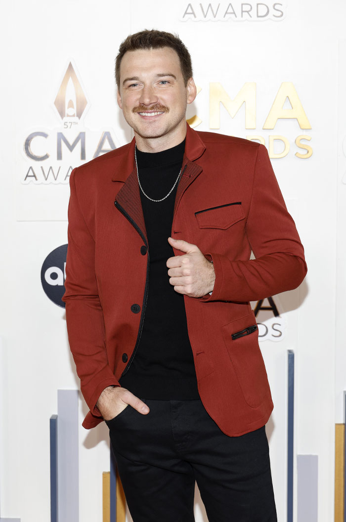 Morgan Wallen in a red jacket at award show, showcasing style and wealth in the music industry.