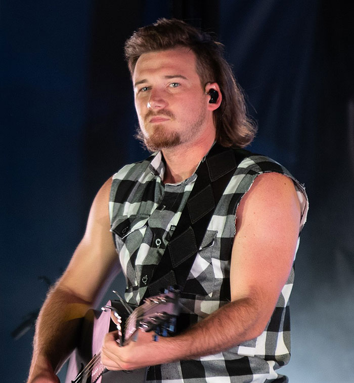 Musician in a sleeveless plaid shirt playing a guitar, related to a "Petulant Move" incident on 'SNL' stage.