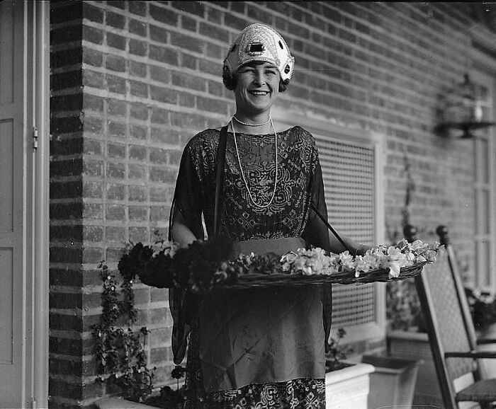 Smiling woman in vintage dress holding a tray of flowers, a rare photograph rescued from glass negatives.