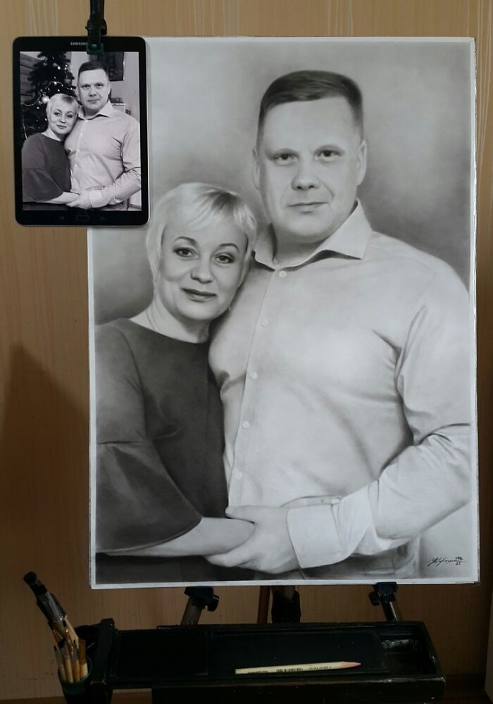 Hyper-realistic pencil portrait of a couple beside a reference photo on a tablet.