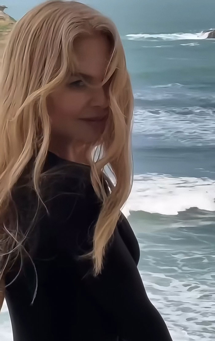 Nicole Kidman by the ocean, wearing black, with long blonde hair blowing in the wind during an outdoor moment.