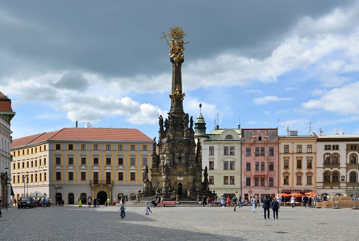 Baroque architectural wonder in a European square, surrounded by colorful historic buildings under a cloudy sky.