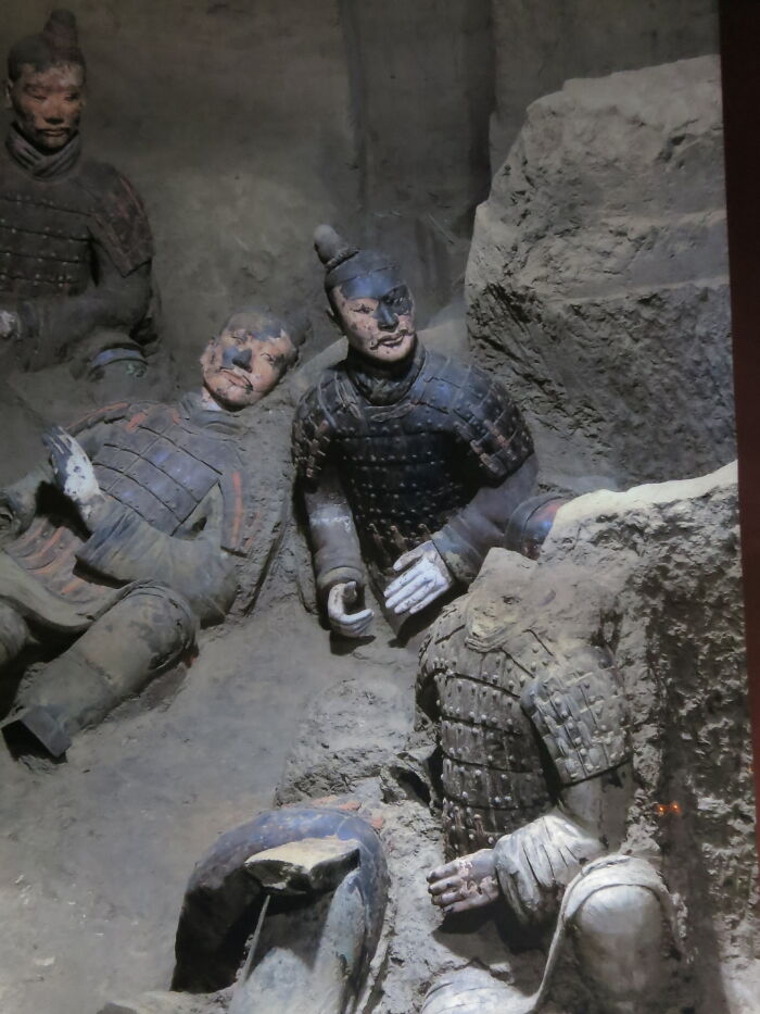 Terracotta warriors partially unearthed in a dimly lit excavation site, showcasing ancient artifacts.