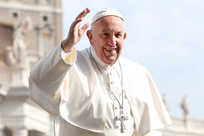 Pope Francis smiling and waving during an outdoor event.