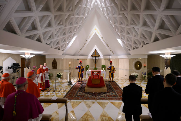 Pope Francis in open casket at Vatican, surrounded by clergy and Swiss Guards in chapel.