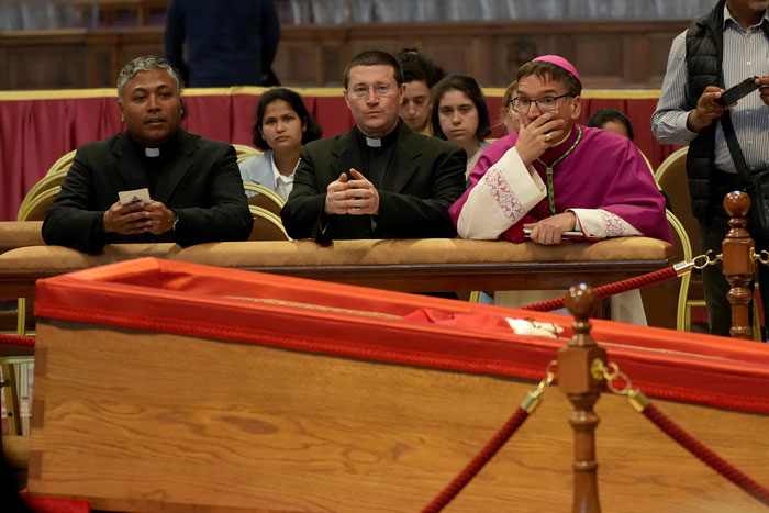 Clergy and attendees beside Pope Francis' open casket in the Vatican, sparking mixed reactions.