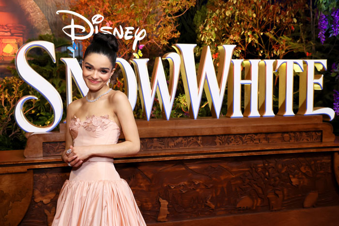 Actress in a pink dress at Disney Snow White event, smiling near a themed backdrop.