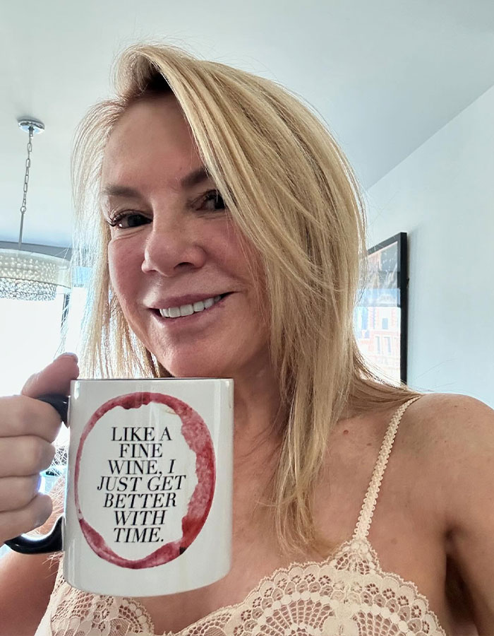 Blonde woman holds a mug with a quote, showing a visibly altered facial appearance, sparking Photoshop controversy.