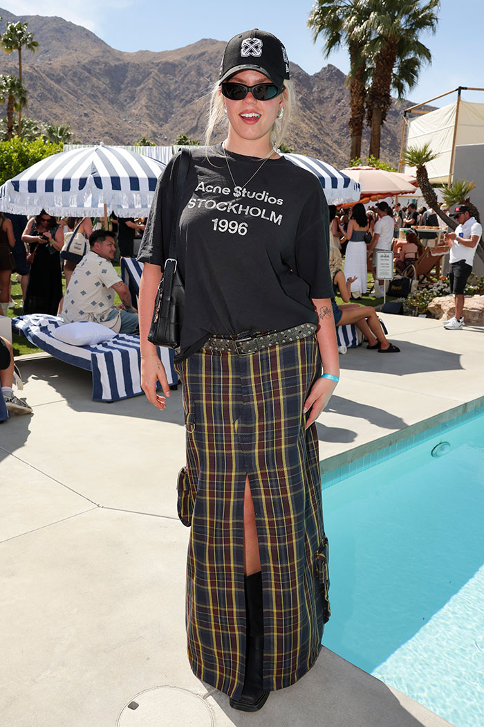 Person at Coachella 2025 in a graphic tee and plaid skirt near a pool, showcasing unique festival fashion.