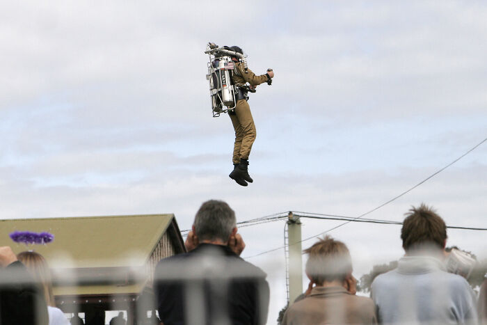 Person using a jetpack, observed by a crowd, showcasing an advanced technology demonstration.