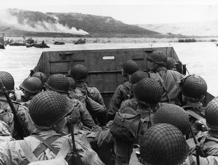 Soldiers in landing craft approach a beach during a historical military operation, predating major events in history.