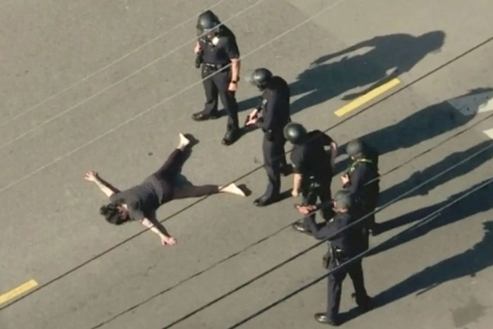 Police in tactical gear surround individual on the ground, aerial view, related to Weezer bassist incident.