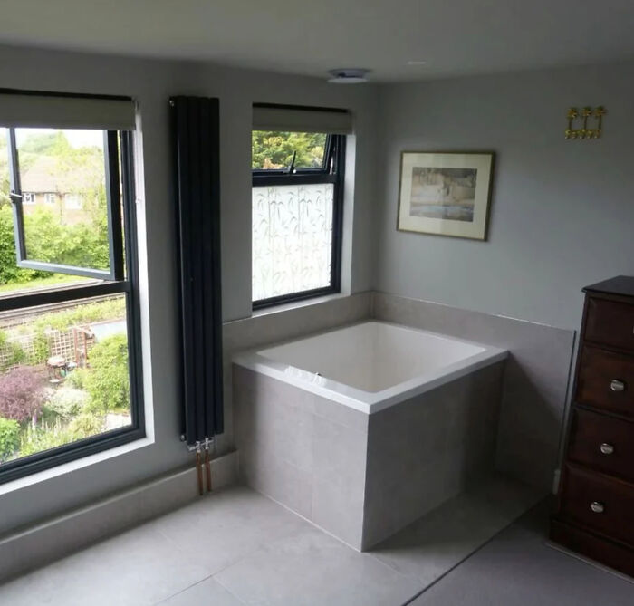 Modern bathroom with a corner vessel sink under two windows, featuring a radiator and wall art.