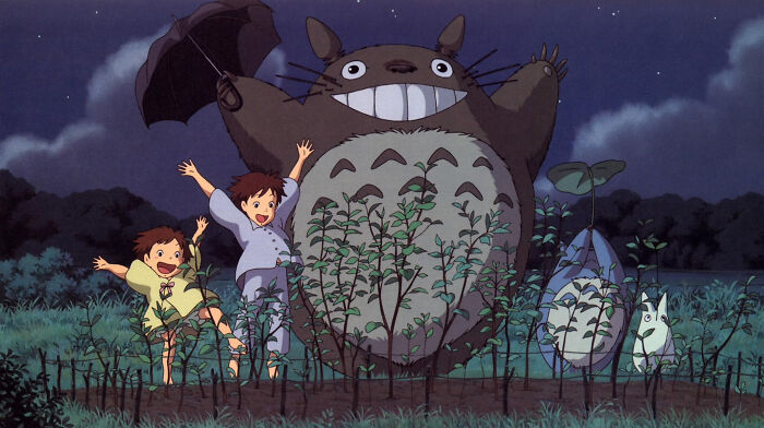 Children happily dancing with Totoro in a magical forest setting.