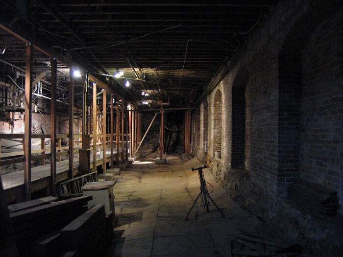 Underground city corridor with brick walls and wooden supports, dimly lit atmosphere.