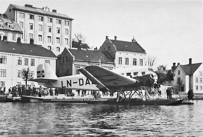 Black and white photo of a seaplane at a European harbor showing life in Europe 100 years ago with historic buildings.