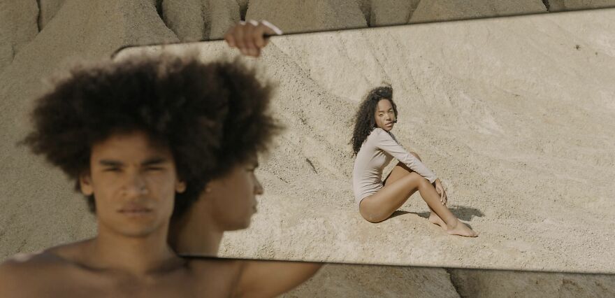 Person holding mirror in a desert, reflecting a woman sitting, illustrating ethical dilemmas visually.