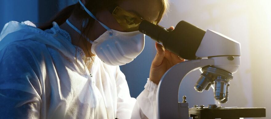 Researcher in lab gear using a microscope, highlighting ethical dilemmas in science.