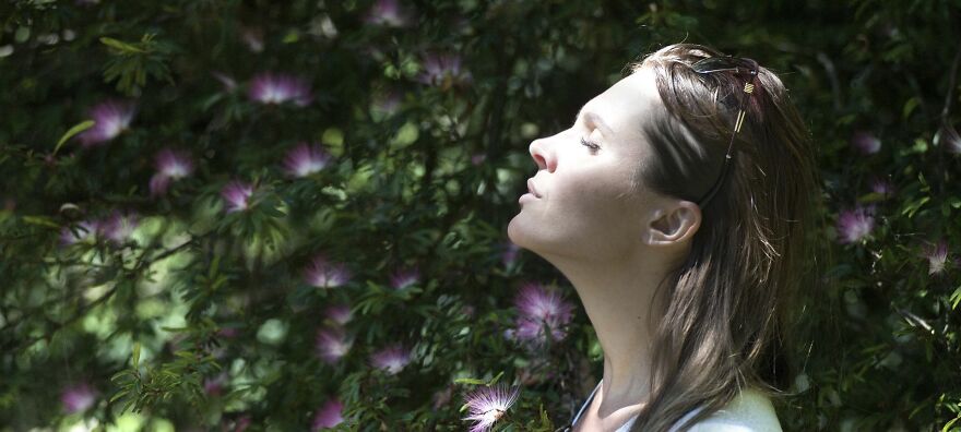 Woman enjoying sunlight, eyes closed in a peaceful garden, surrounded by flowers, illustrating ethical dilemmas.