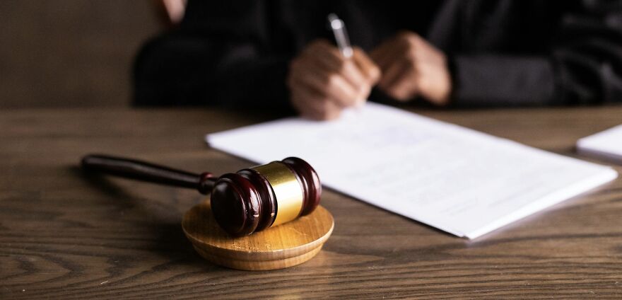Gavel on a table with a person writing in the background, symbolizing ethical dilemmas and decision-making.