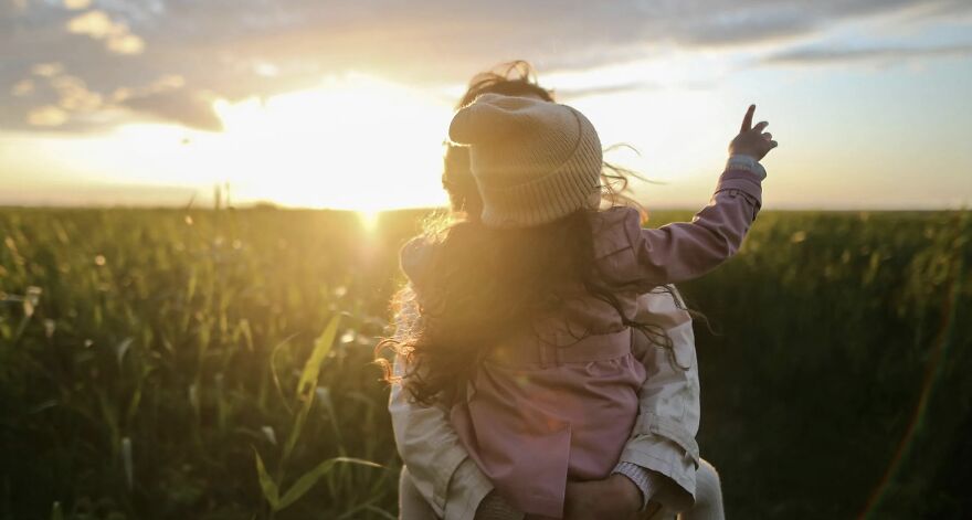 Child in a hat being carried through a field at sunset, representing ethical dilemmas.