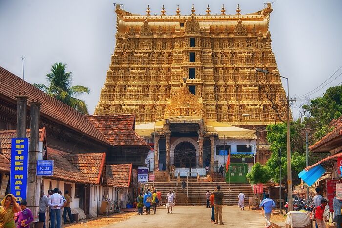 Golden temple facade showcasing intricate architectural wonders, with people walking in a bustling street scene.