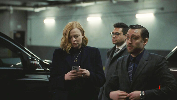 Three people in a dimly lit parking garage, one with a phone, possibly from a 10/10 show.