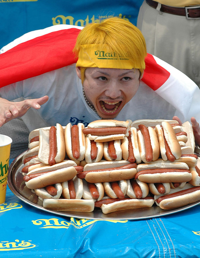 A person with real-life superpowers, ready to eat a large stack of hot dogs in a competitive setting.