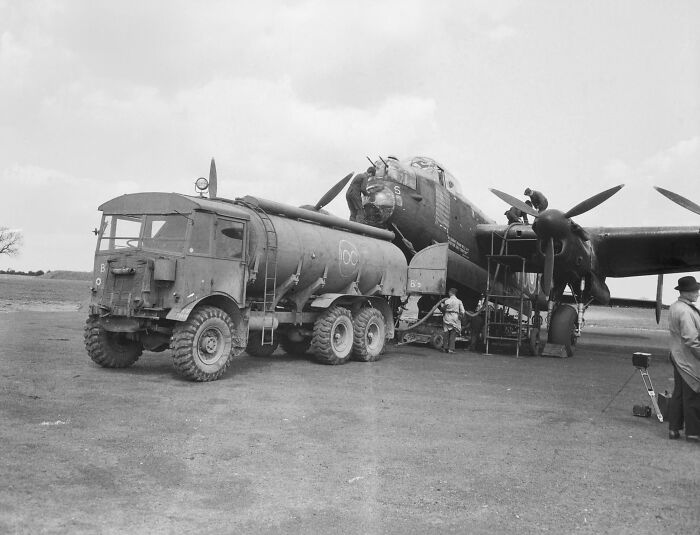 Tanker truck refueling a WWII aircraft, with crew members working on the plane.