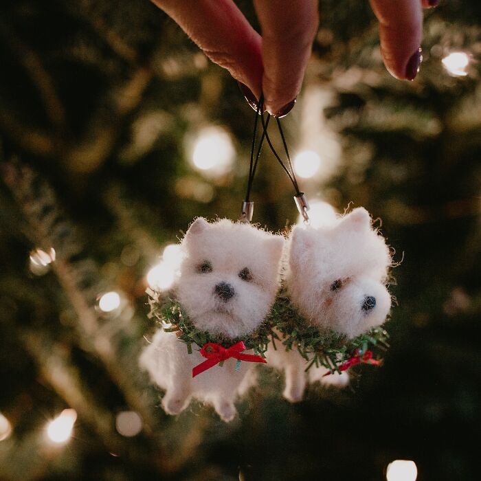Hand holding cute felted pet ornaments, featuring two fluffy dogs with festive decorations.