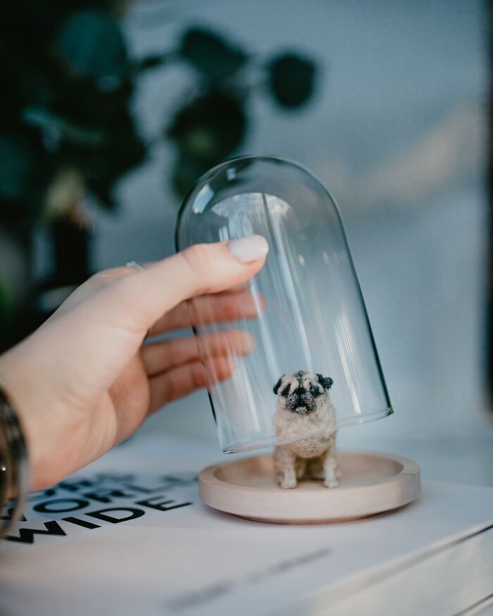 Hand placing glass dome over cute felted pet sculpture, showcasing adorable artistry.