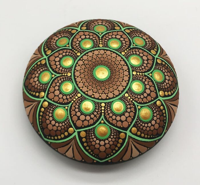 Beautiful mandala design painted on a round stone, featuring intricate patterns in green, gold, and brown.