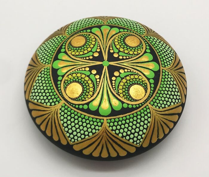 A beautifully intricate mandala painted on a stone, featuring green and gold patterns.