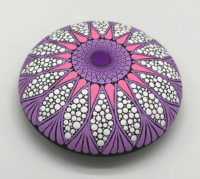Colorful mandala art painted on a smooth stone, featuring intricate patterns in purple and pink hues.