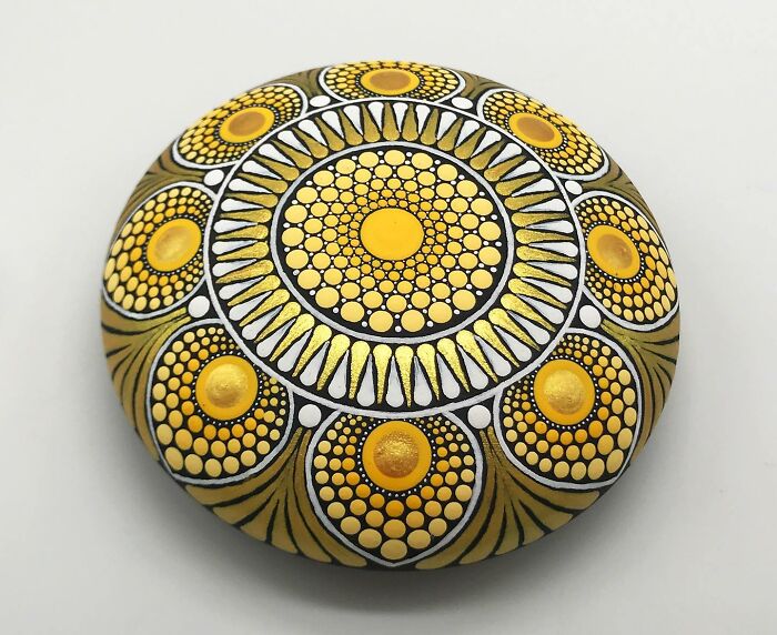 Stone with a beautiful mandala design in vibrant yellow and gold hues against a plain background.