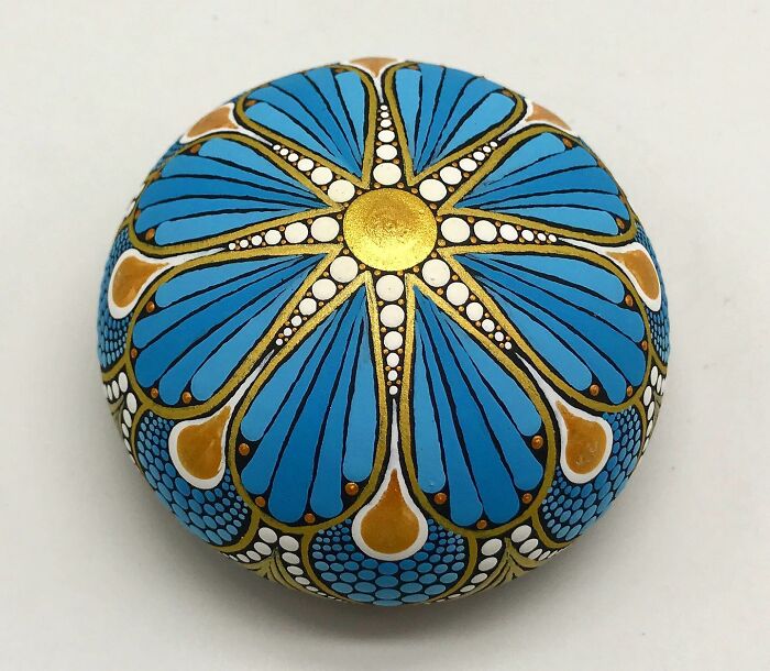 Beautifully painted mandala stone, featuring intricate designs in blue, gold, and white.