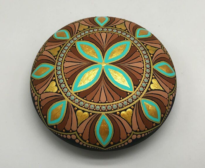 Beautiful mandala art on a stone, featuring intricate turquoise, gold, and brown patterns.